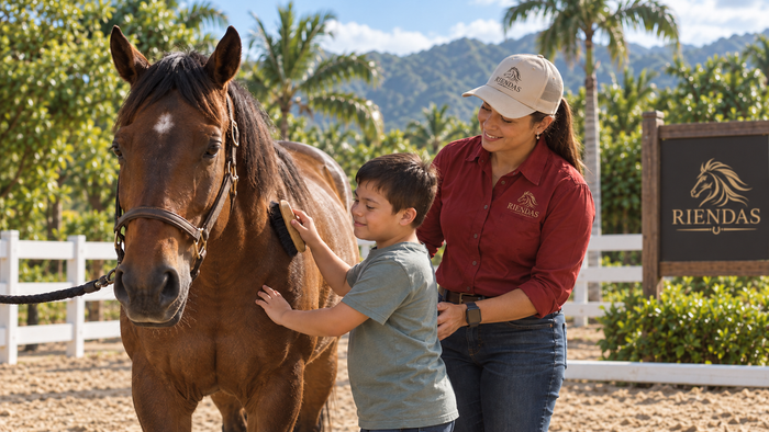Niño interactuando con un caballo desde el suelo acompañado por una profesional de RIENDAS durante una experiencia de Equinoterapia.